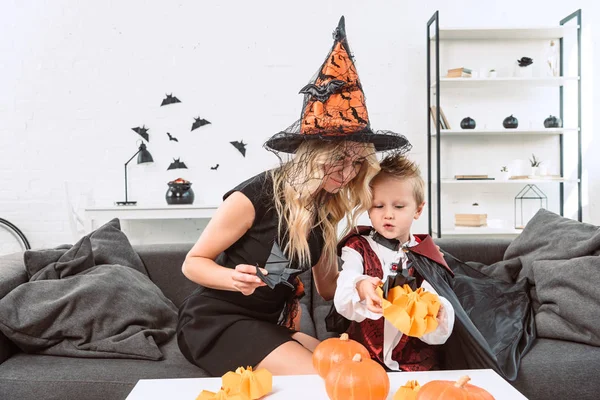 Mother and little son in halloween costumes with black paper bats on sofa at home — Stock Photo