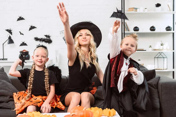 Portrait de mère et d'enfants en costumes d'Halloween jetant des chauves-souris en papier noir à la maison — Photo de stock