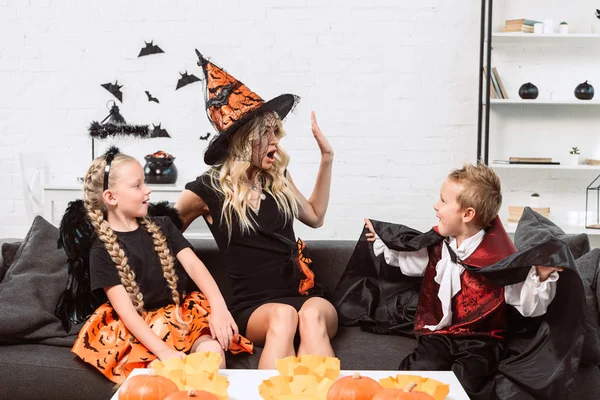 Ritratto di mamma emotiva e bambini in costume di Halloween seduti sul divano di casa — Foto stock