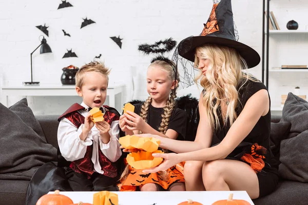 Ritratto di mamma e bambini in costume di Halloween seduti sul divano di casa — Foto stock