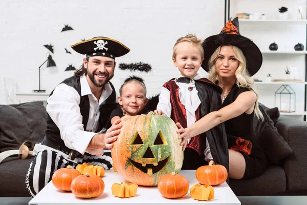 Ritratto di famiglia sorridente in vari costumi di Halloween a tavolino con zucche a casa — Foto stock