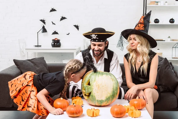 Семья в костюмах на Хэллоуин на диване за кофейным столиком с тыквами дома — стоковое фото