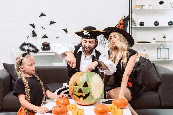 Family in halloween costumes on sofa at coffee table with pumpkins at home — Stock Photo