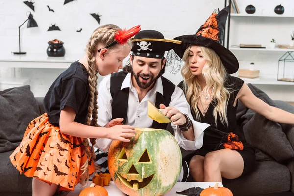 Familia en trajes de Halloween en el sofá en la mesa de café con calabazas en casa - foto de stock