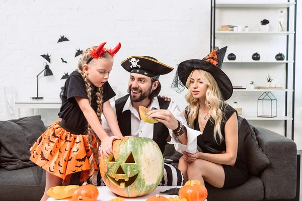 Familie in Halloween-Kostümen auf Sofa am Couchtisch mit Kürbissen zu Hause — Stockfoto