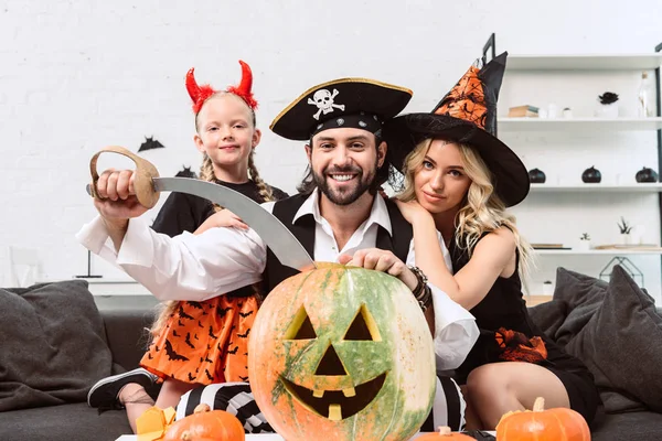 Familie in Halloween-Kostümen auf Sofa am Couchtisch mit Kürbissen zu Hause — Stockfoto