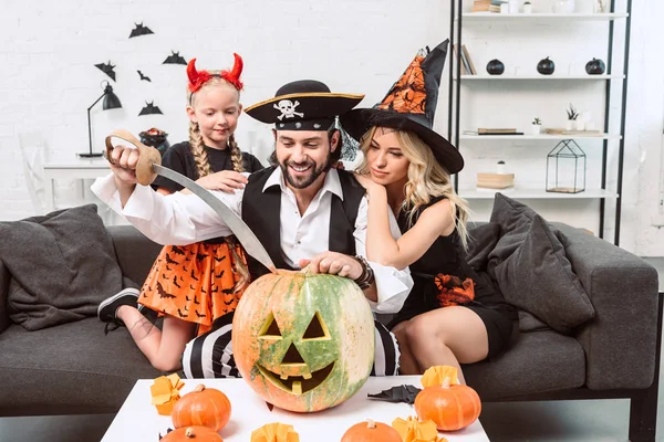 Familia en trajes de Halloween en el sofá en la mesa de café con calabazas en casa - foto de stock