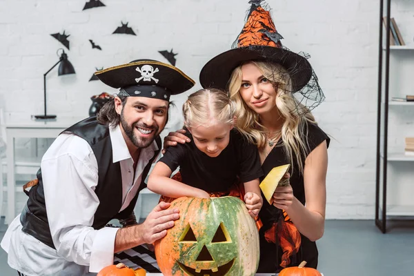 Retrato de los padres y la pequeña hija en trajes de Halloween en la mesa con calabazas en casa - foto de stock