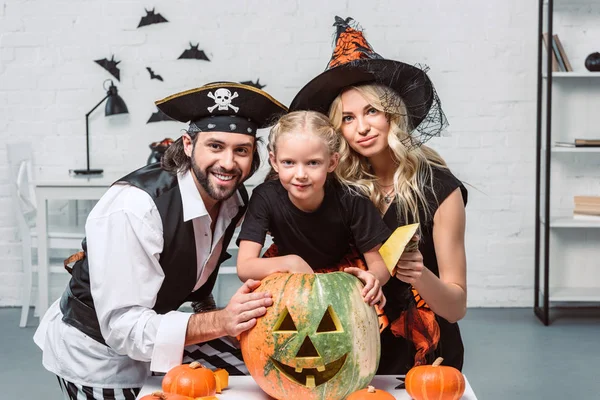 Retrato de los padres y la pequeña hija en trajes de Halloween en la mesa con calabazas en casa - foto de stock