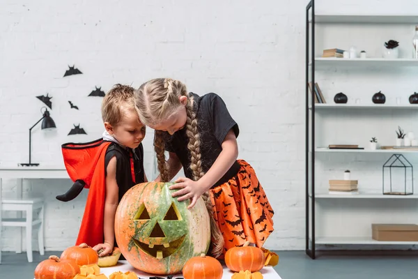 Little kids in halloween costumes looking into pumpkin at home — Stock Photo