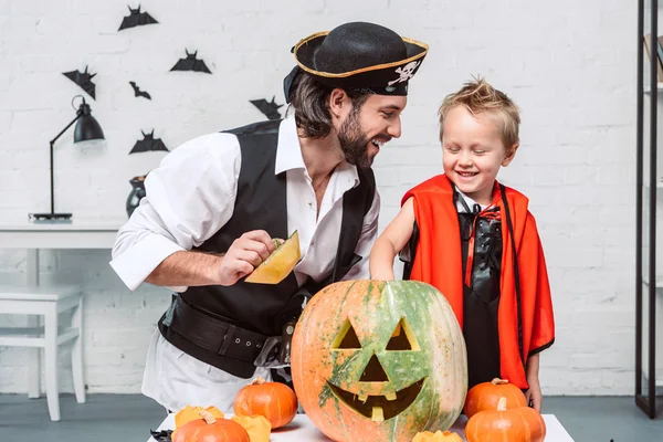 Glücklicher Mann im Piratenkostüm und Sohn im Vampir-Halloween-Kostüm mit Kürbis zu Hause — Stockfoto