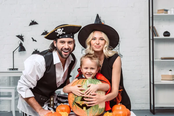 Retrato de padres felices e hijo en trajes de Halloween en la mesa con calabazas en casa - foto de stock