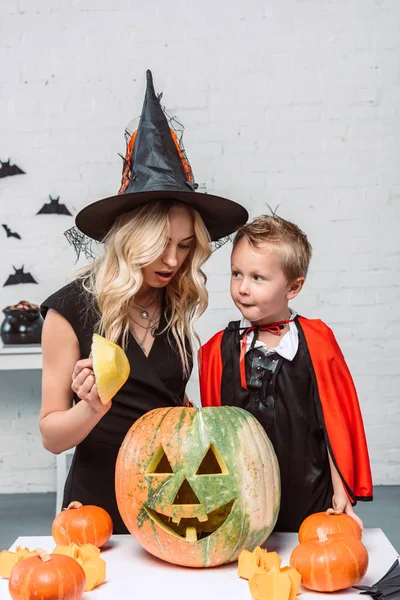 Retrato de la madre y el hijo en trajes de Halloween en la mesa con calabazas en casa - foto de stock