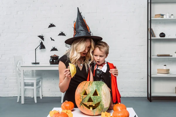 Portrait of shocked mother and son in halloween costumes looking into pumpkin together — Stock Photo