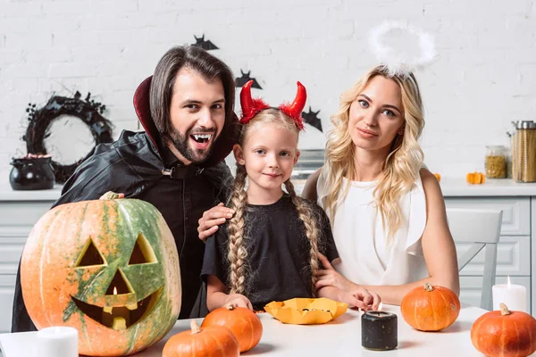 Retrato de la familia en trajes de Halloween en la mesa con calabazas en la cocina en casa - foto de stock