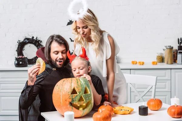 Ritratto di famiglia in costumi di Halloween guardando insieme in zucca in cucina a casa — Foto stock