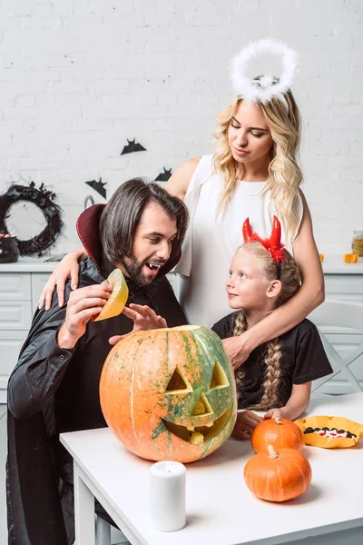 Retrato de la familia en trajes de Halloween en la mesa con calabazas en la cocina en casa - foto de stock