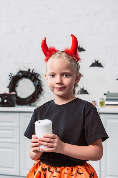 Portrait of little kid with red devil horns holding candle in hands at home, halloween holiday concept — Stock Photo