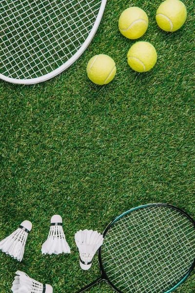 Вид сверху на бадминтон и теннисное оборудование, устроенное на зеленой лужайке — стоковое фото