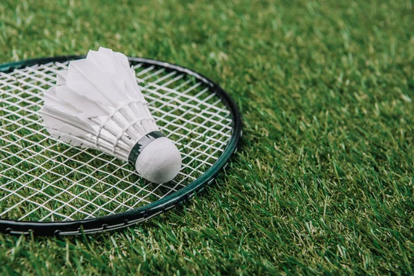 Close up view of white shuttlecock and badminton racket lying on green grass — Stock Photo