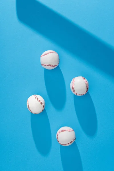 Top view of arranged baseball balls and bat shadow on blue background — Stock Photo