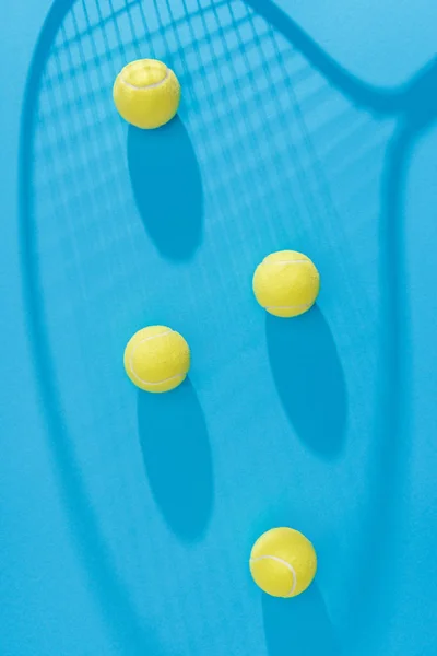 Top view of arranged tennis balls and racket shadow on blue backdrop — Stock Photo