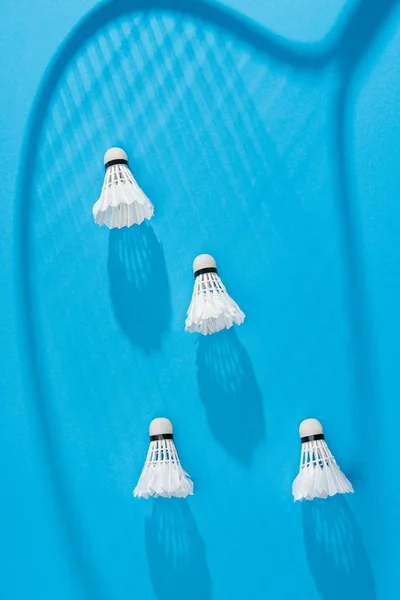 Vista dall'alto di navette bianche e ombra racchetta badminton su sfondo blu — Foto stock