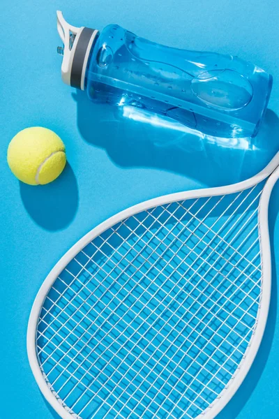 Vista de cerca de la botella de agua deportiva y el equipo de tenis en el fondo azul - foto de stock