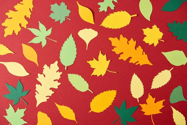 Flache Lage mit bunten papiergefertigten Blättern auf rotem Hintergrund — Stockfoto