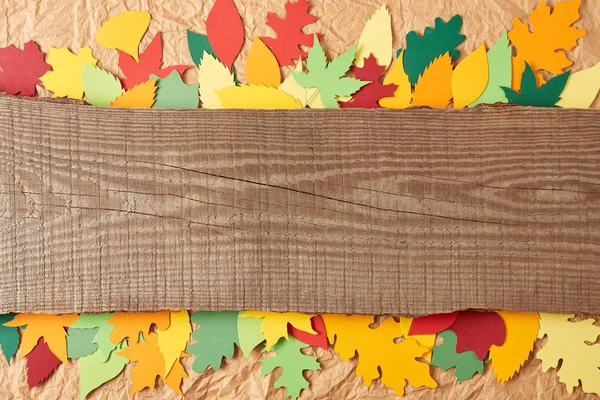 Top view of wooden plank and colorful paper leaves arrangement on crumpled paper backdrop — Stock Photo