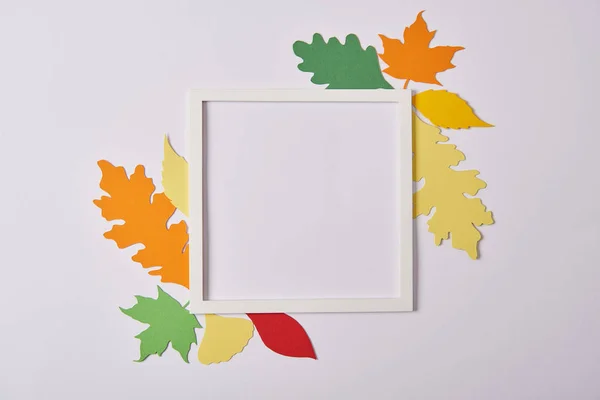 Плоский укладка с бумажными листьями ручной работы и пустой рамой на белом столе — стоковое фото