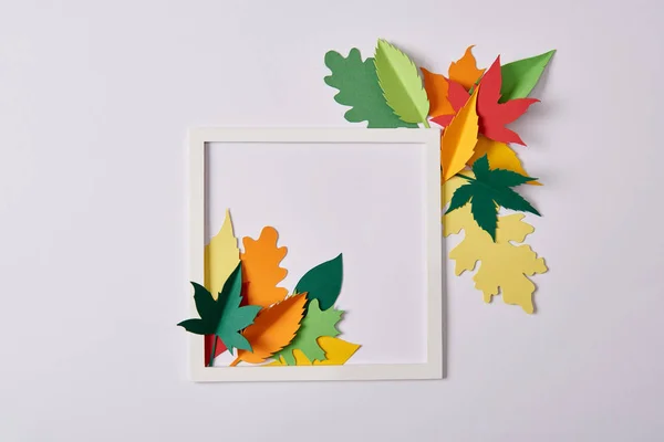 Flat lay with handcrafted paper leaves and white frame on white tabletop — Stock Photo