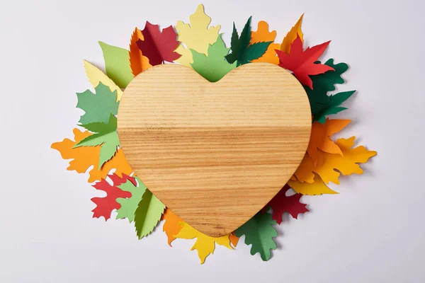 Top view of wooden heart shaped board and colorful handcrafted leaves on white surface — Stock Photo