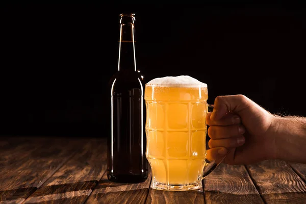 Imagem cortada de homem clinking caneca com garrafa de cerveja na mesa de madeira — Fotografia de Stock