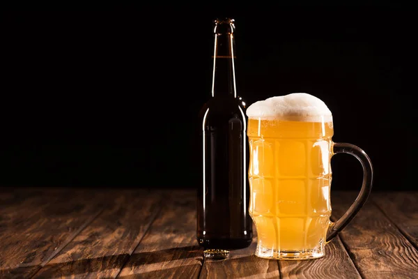 Botella de cerveza y taza de cerveza ligera fresca con espuma en la mesa de madera, concepto minimalista - foto de stock