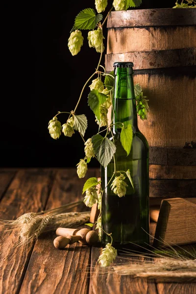 Bierflasche, Weizen, Hopfen und Holzfass am Tisch auf schwarzem Hintergrund — Stockfoto