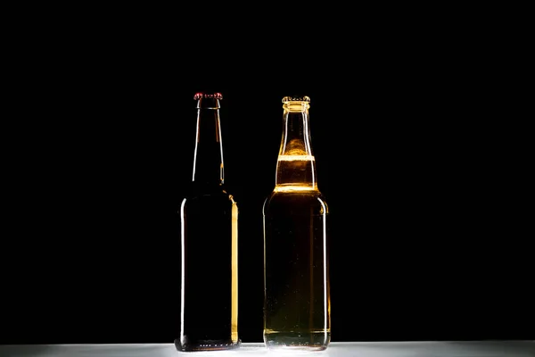 Garrafas de cerveja claras e escuras à mesa sobre fundo preto, conceito minimalista — Fotografia de Stock