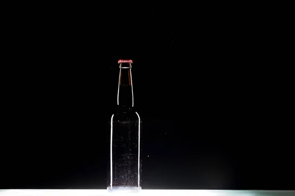 Garrafa de cerveja escura à mesa no fundo preto, conceito minimalista — Fotografia de Stock