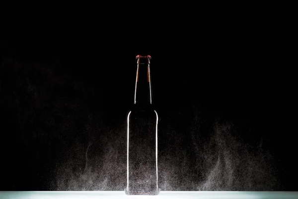 Бутылка пива с брызгами воды на поверхности на черном фоне — стоковое фото