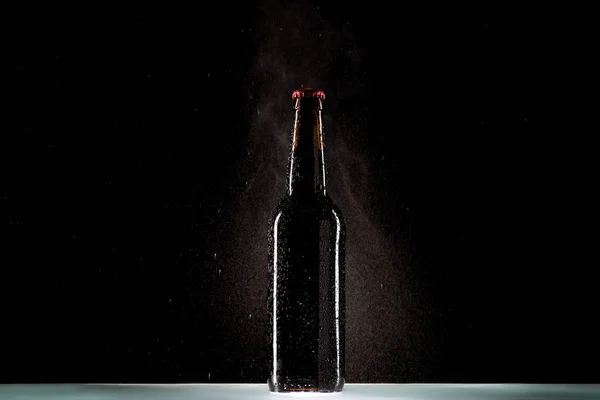 Bottle of beer with spraying water at table on black background — Stock Photo