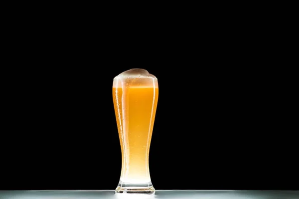 Vaso de cerveza fresca con espuma en la mesa sobre fondo negro, concepto minimalista - foto de stock