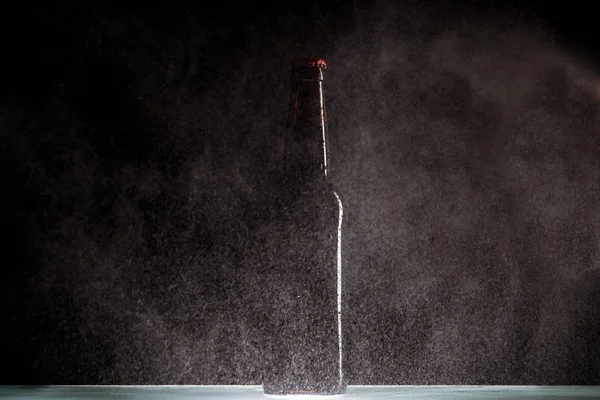 Selective focus of beer bottle with spraying water around at surface on black background — Stock Photo