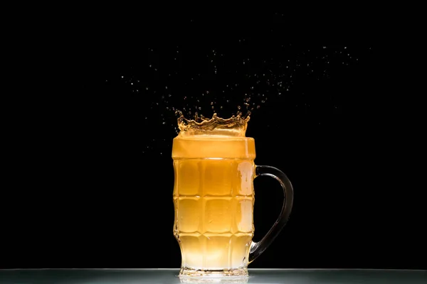 Glass of light beer with splashes at table on black background, minimalistic concept — Stock Photo