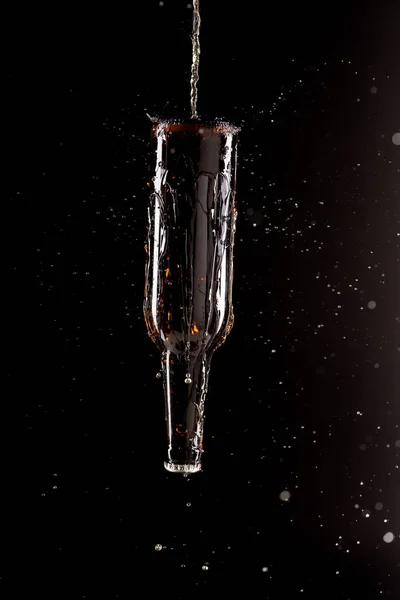 Selective focus of beer pouring on bottle upside down with splashes around isolated on black background — Stock Photo