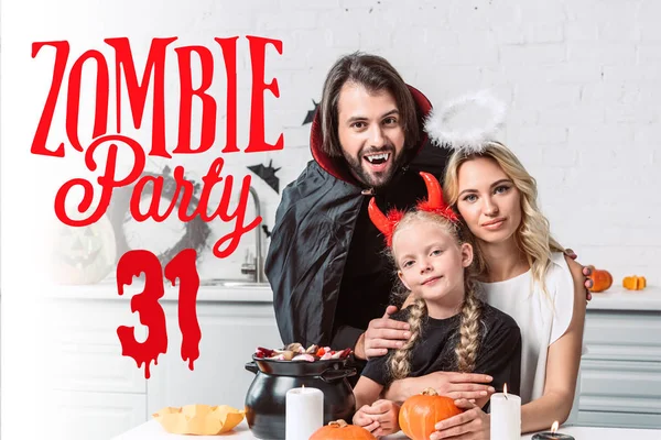 Portrait of parents and daughter in halloween costumes at table with treats in black pot in kitchen at home with 