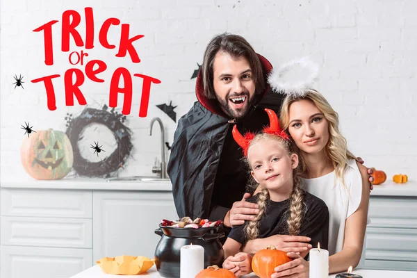 Ritratto di genitori e figlia in costume di Halloween a tavola con dolcetti in pentola nera in cucina a casa con scritte 
