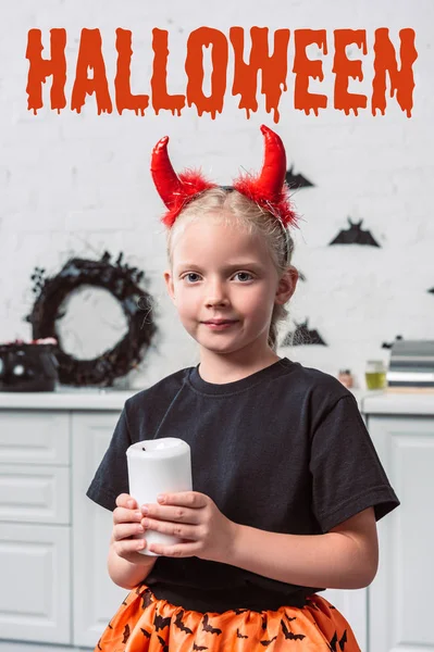 Ritratto di bambino con le corna rosse del diavolo che tengono la candela in mano a casa, con scritta 