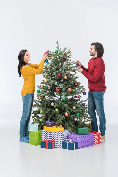 Pareja sonriente decorando árbol de navidad con bolas de vidrio aisladas en blanco - foto de stock