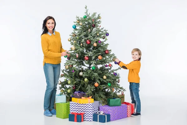 Mère heureuse avec fils décorant arbre de Noël avec des boules de verre et regardant la caméra isolée sur blanc — Photo de stock