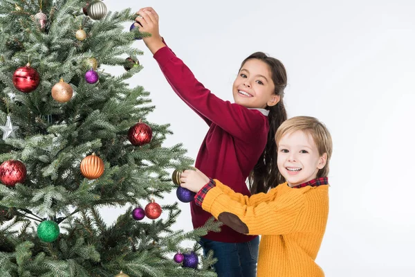 Felices hermanos decorando árbol de navidad con bolas de vidrio aisladas en blanco - foto de stock